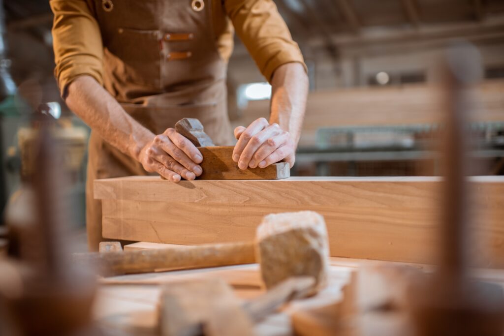 Carpenter working with a wood, planing a bar with a plane in the carpentry workshop. Close-up on hands